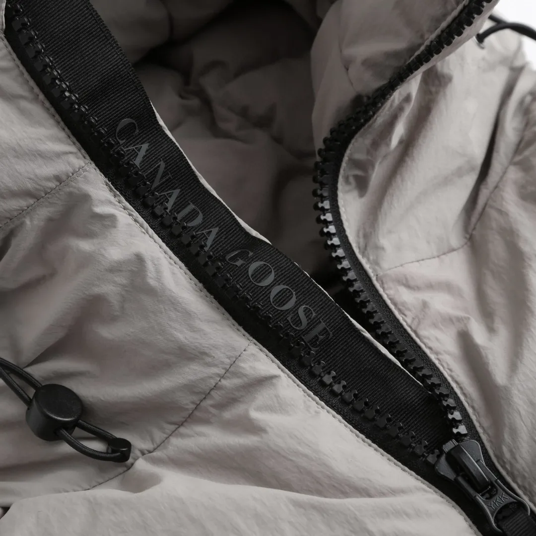 P1010 [Exclusive supply] Canada Goose Black Label Badge Hooded Down Jacket (Khaki) The high-quality filling is made of 90 national standard high-quality white duck down, selected high-loft velvet, weighing 240g, light and warm, with excellent temperature locking performance and good resilience. The fabric is woven with 400T high-count yarn. After special water-repellent treatment, the surface forms a lotus leaf effect - raindrops will slide down like beads, and snow particles will fall off when touched. The tear resistance reaches 200N (approximately 20kg load-bearing), the light gray matte texture breaks the stereotype of "outdoor clothing = hardcore", and the soft luster presents a high-end matte effect under urban neon lights, seamlessly switching scenes from ski resorts to CBD office buildings. The ribbon is woven with polyester as the base, and the brand letters are decorated on the ribbon through high-precision computer embroidery. The edges of the pattern are clear, the stitches are fine and even, and multiple layers of embroidery thread are stacked to enhance the three-dimensional effect. Precision thread reinforcement prevents linting and ensures the fluffy and resilient elasticity lasts as new. The embedded cuffs are three-dimensionally woven to form a "wavy" elastic structure, which forms natural folds when fitting the wrist, increasing the contact area with the skin, thus improving the windproof effect. At the same time, micro-velvet treatment is added to the inside of the cuffs, which feels like a second layer of skin and avoids friction on the skin from metal zippers or hard fabrics. Size:S-M-L-XL